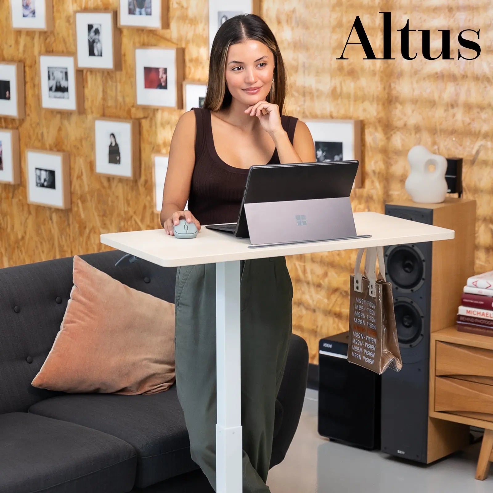 Woman stands at a white mobile desk, engaging with a laptop in an office environment decorated with framed pictures and a plant, exuding a relaxed yet productive atmosphere.