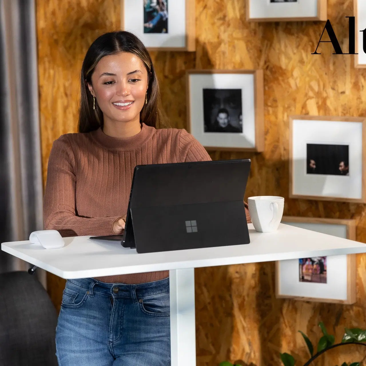 Woman seated at a white mobile desk, engaging with a laptop in an office environment decorated with framed pictures and a plant, exuding a relaxed yet productive atmosphere.