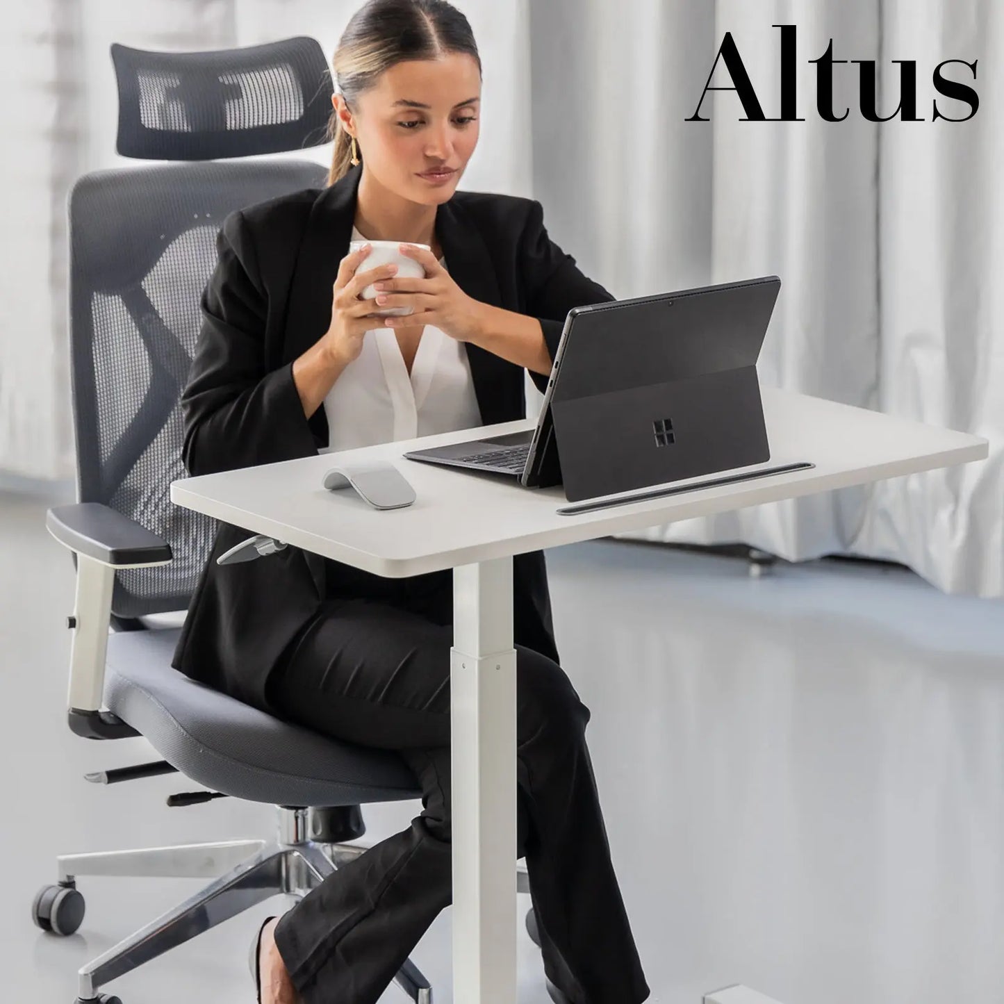 A professional setting with a woman seated at a modern, white standing desk, working on a laptop, with a neutral-toned office chair and background.