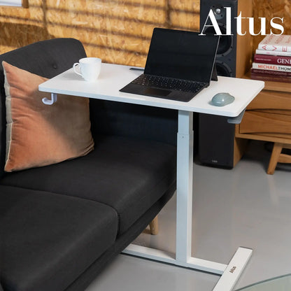 A workplace environment with a woman typing on a laptop at a white standing desk, with personal and decor elements around, reflecting a modern and functional office space.