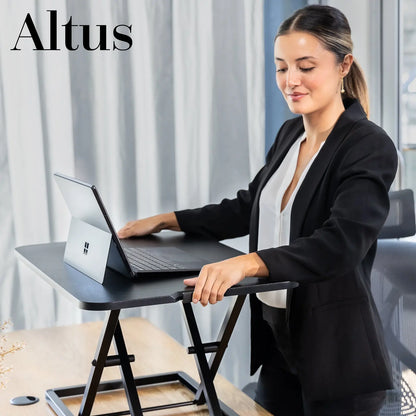 Close-up view of a woman using a laptop on a black sit-stand desk converter in a modern office setting.