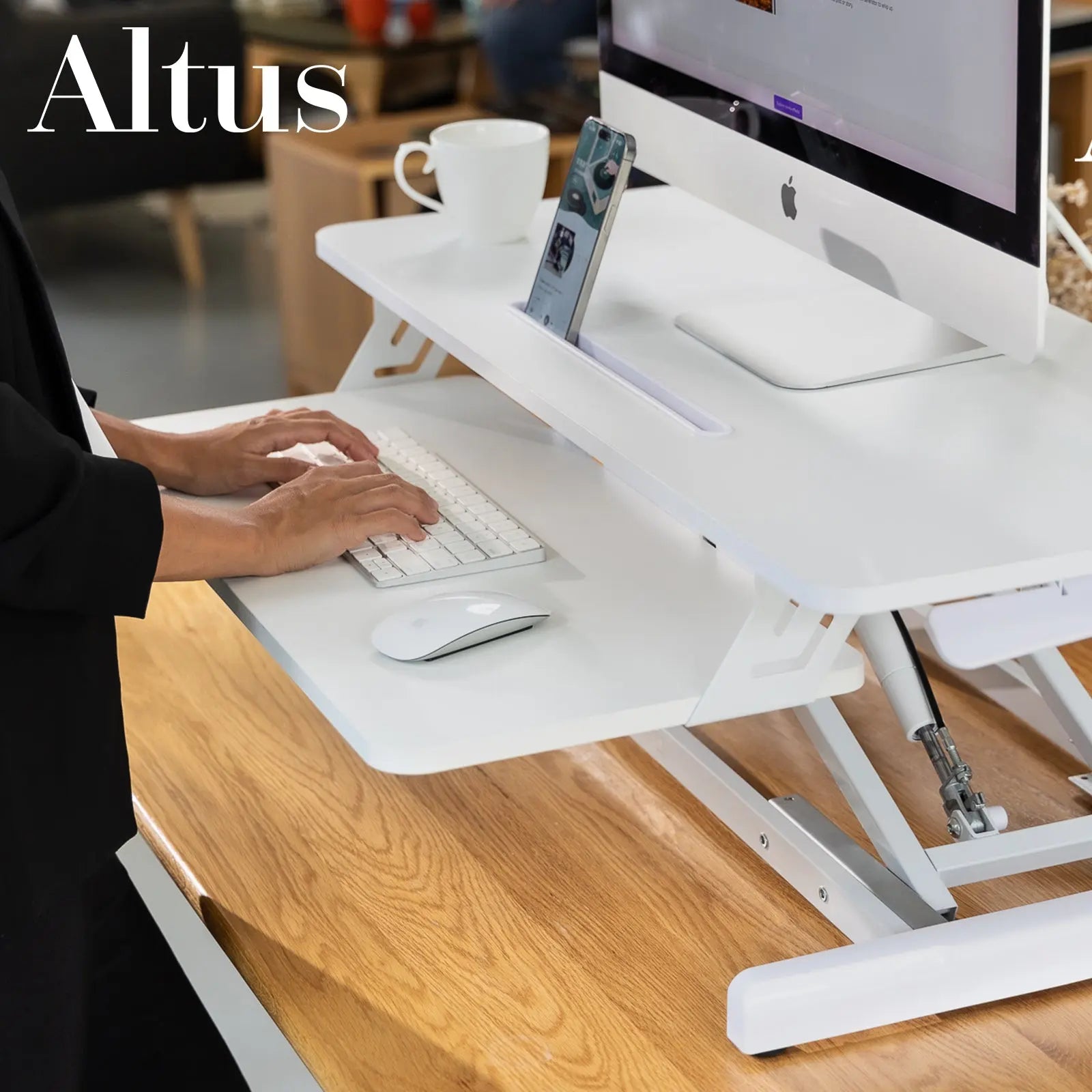 Woman typing on a keyboard at a white desk converter, focusing on work with an iMac and a phone on the side.