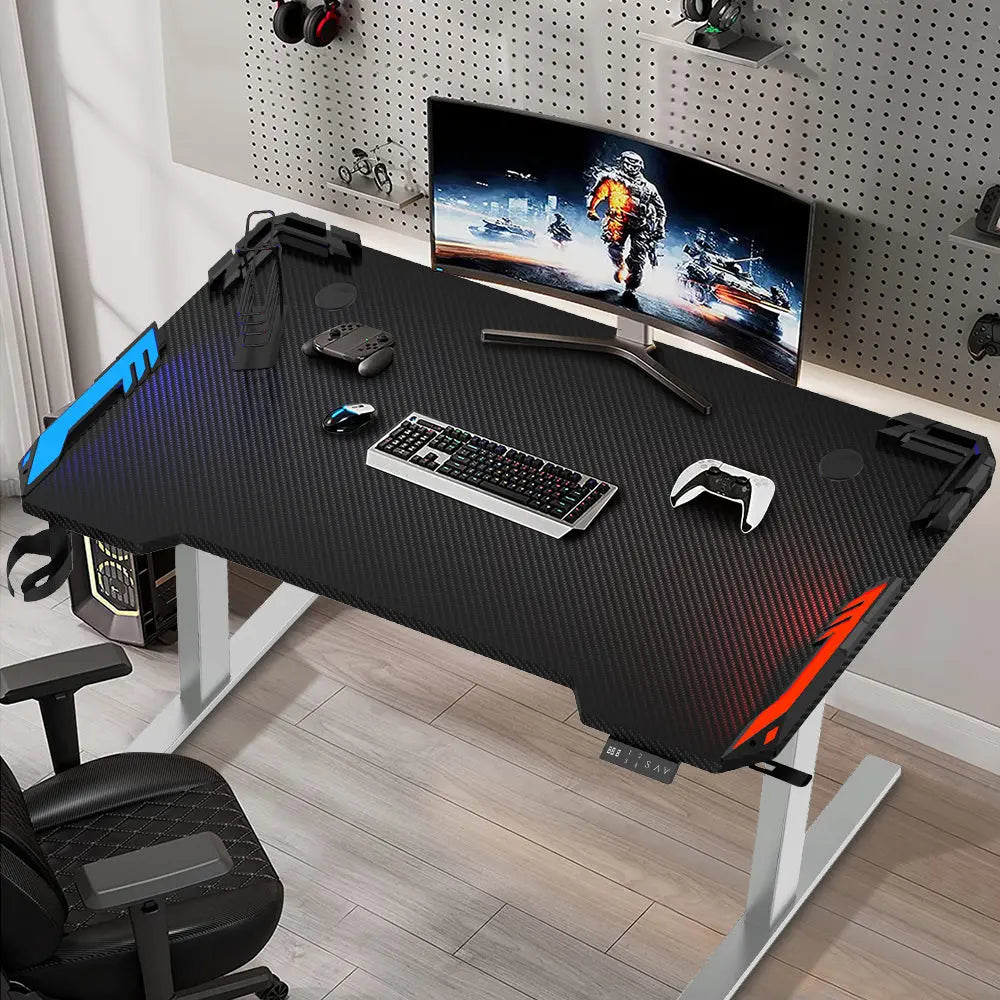 A gaming setup featuring the height-adjustable desk with gaming accessories like headphones, a controller, and dual monitors, placed in a modern room with tool walls for additional gaming equipment.